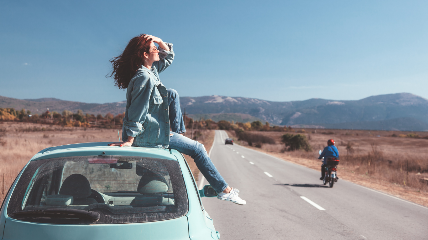 Woman sitting on a blue car at the side of a road